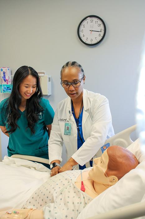 A nursing instructor teaches a nursing student technique on a medical maniken.